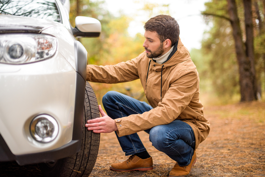 a guy checking the front left wheel of his car. One of the things you need to check before renting a car.