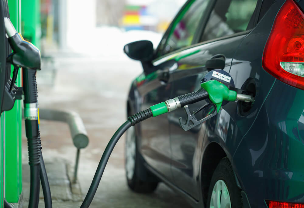 a gas pump putting a fuel into a black car. An important thing to check before renting a car.